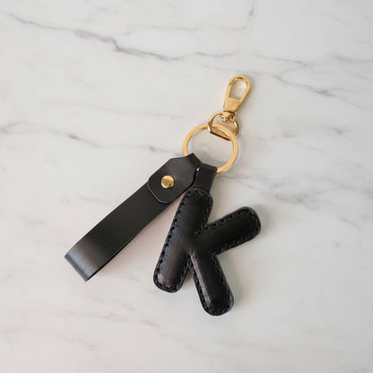A Black leather keychain charm with letter 'K' and a loop and with a gold-tone lobster clasp and split ring.